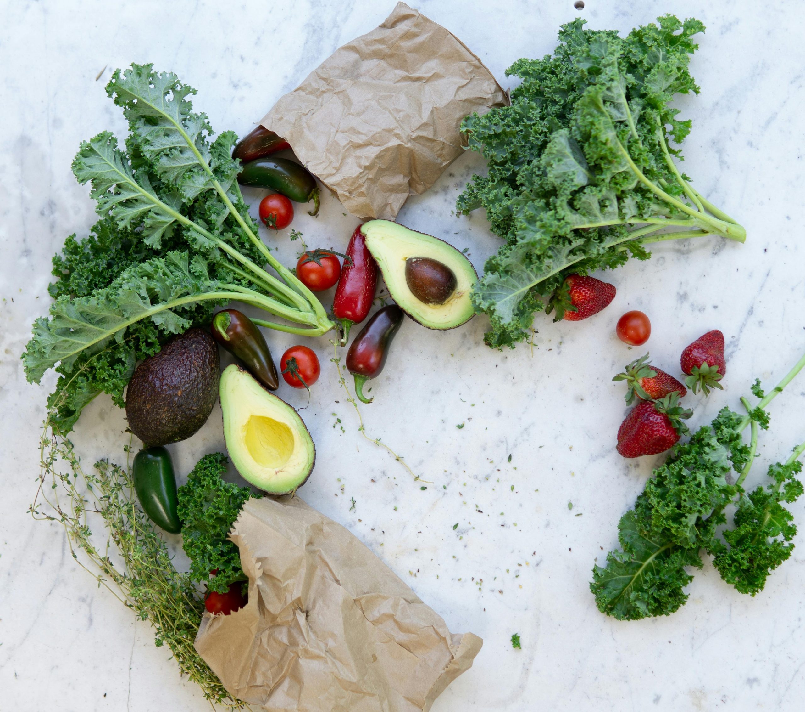 Vue épurée d'avocats et de poivrons rouges disposés sur un plan en marbre blanc, illustrant un article sur l'équilibre nutritionnel et la vitalité cellulaire des leaders.